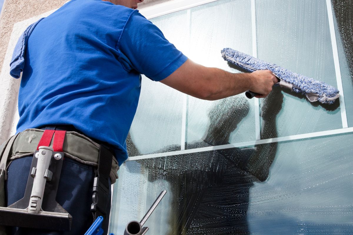 A man wearing a blue shirt cleans a window with a squeegee, focusing on achieving a streak-free finish.