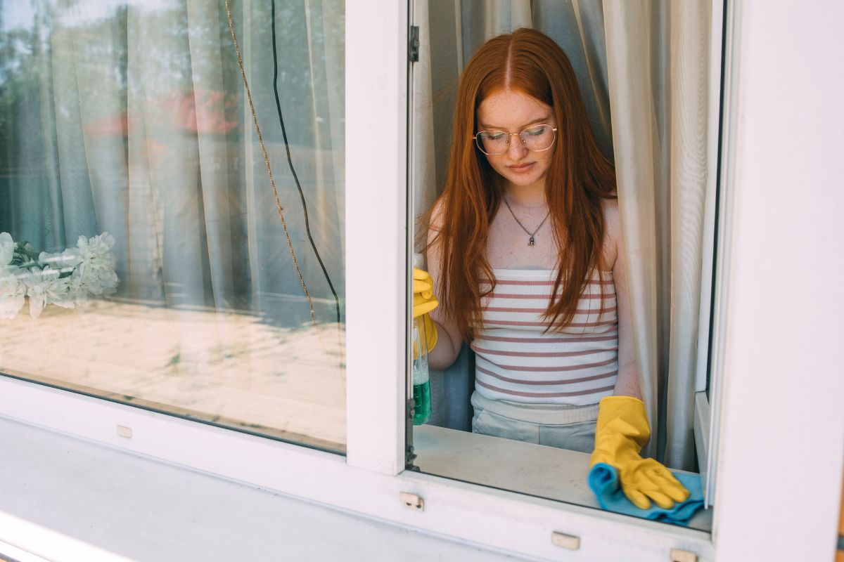 A woman in rubber gloves cleans a window, wearing a yellow glove on her right hand for added protection. 