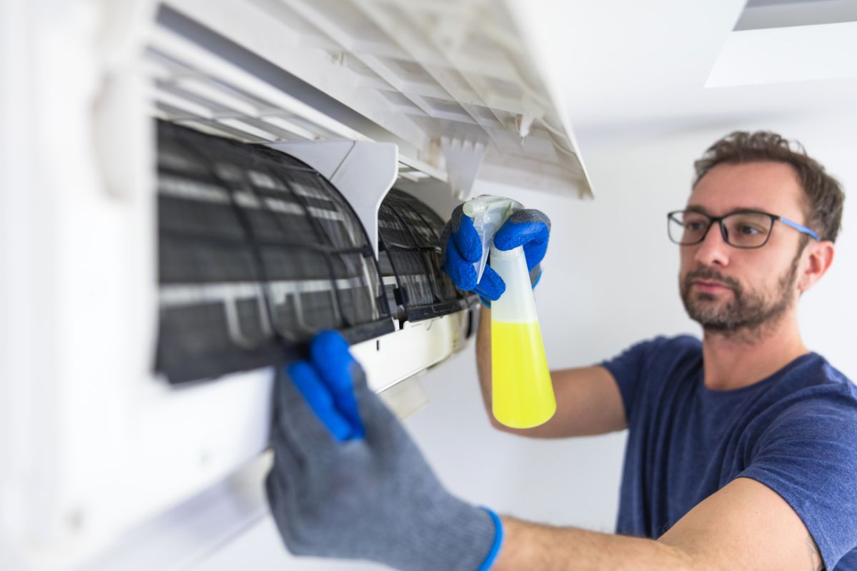  A man with glasses is diligently cleaning an air conditioner, ensuring it operates efficiently. 